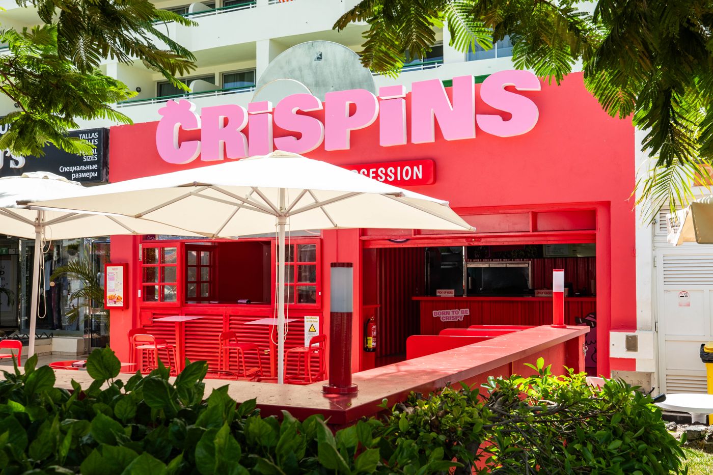 Fachada roja de Crispins con rótulo rosa y terraza con sombrillas