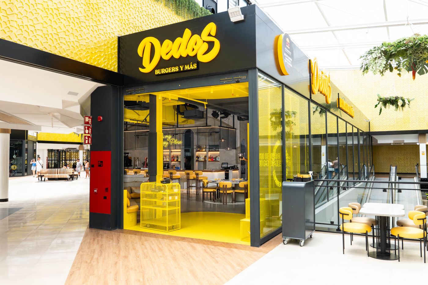 Fachada de Dedos en el centro comercial La Gran Manzana, con rótulo amarillo y cerramiento de vidrio